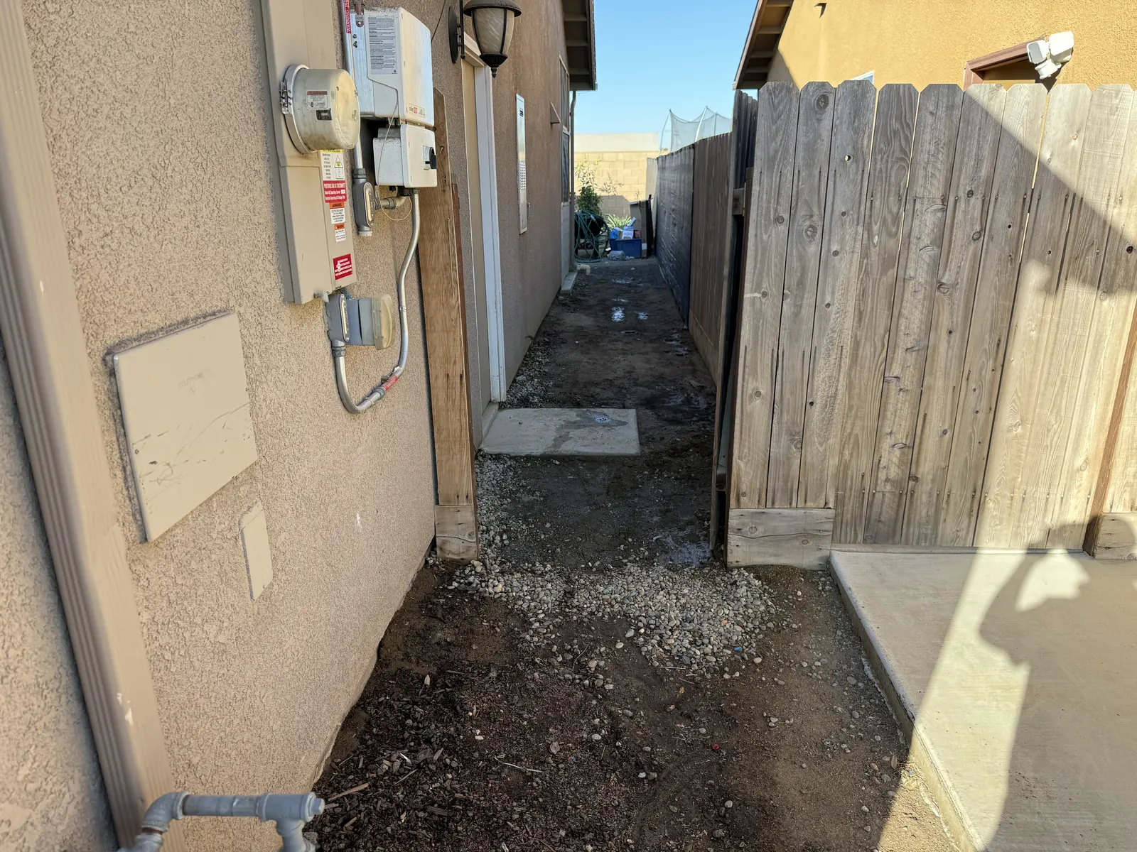 Narrow side yard of bare dirt and gravel, utility meters mounted on the wall