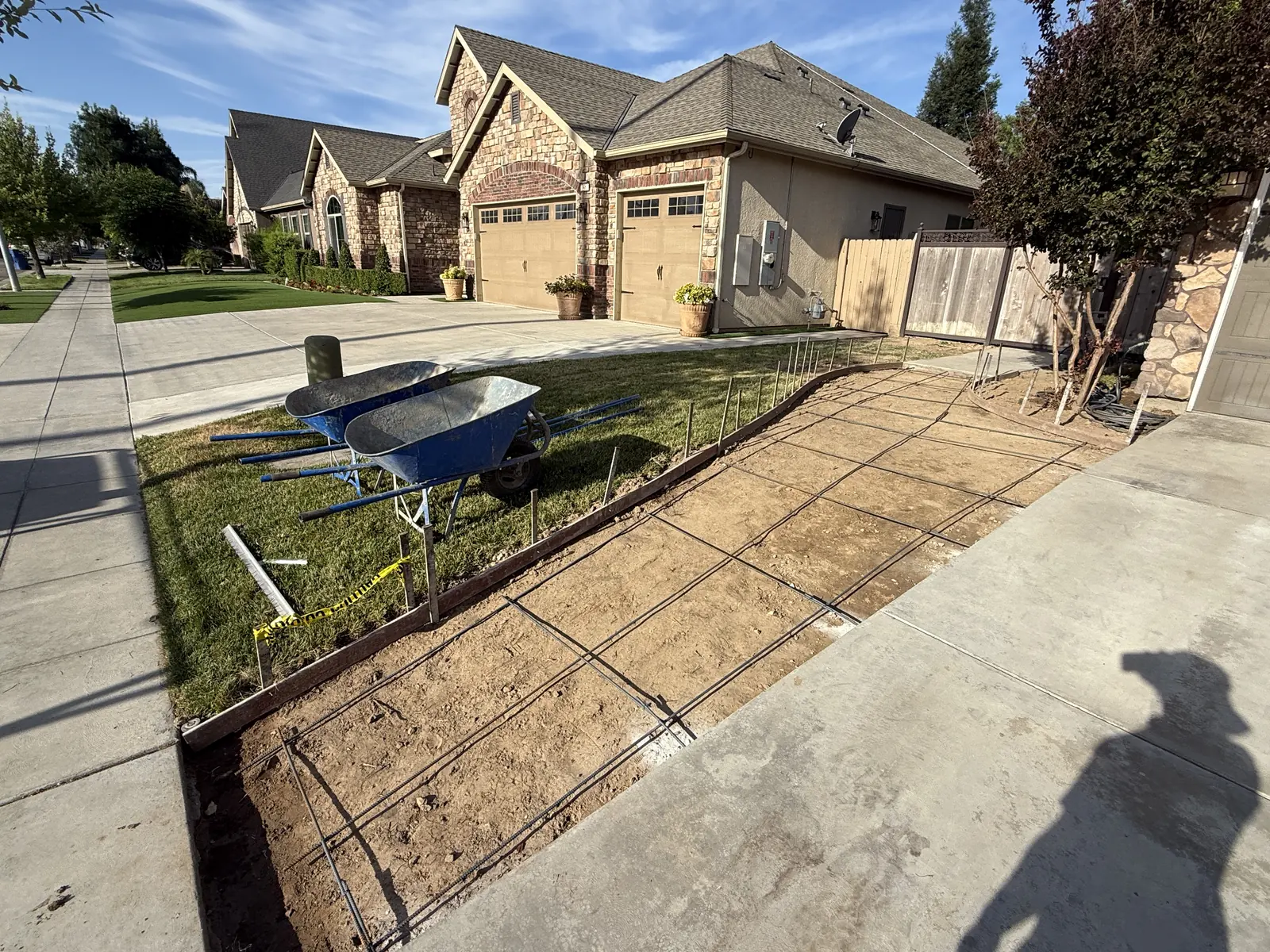 Reinforcing mesh tied inside wood forms beside a driveway, wheelbarrows parked on the grass
