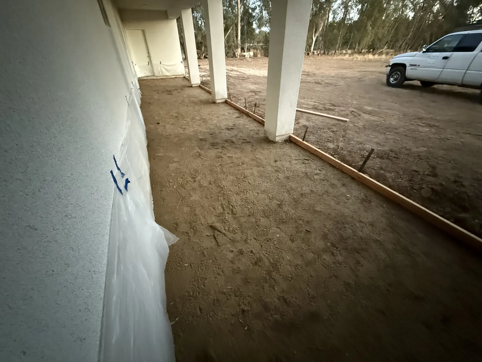 Wood forms set along a covered walkway ahead of the pour, work truck parked on the dirt