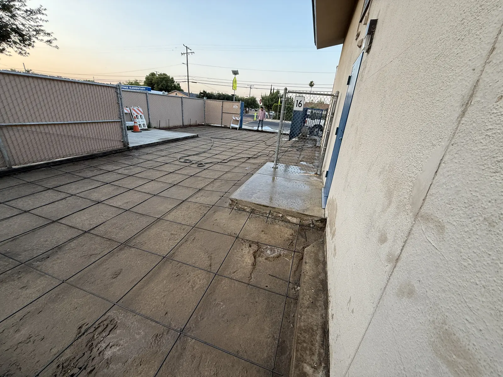Reinforcing mesh covering the ground along a classroom wall, gate standing open to the street