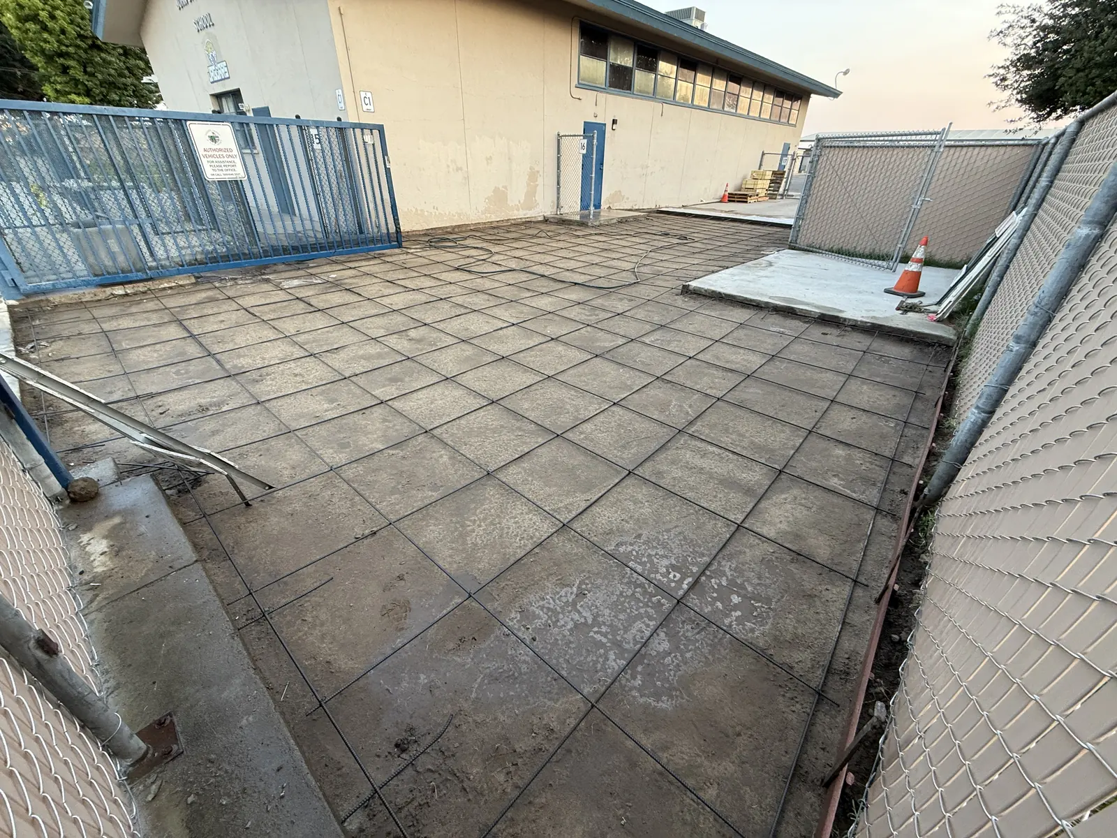 Wire mesh laid over compacted base in a fenced school service yard before the pour