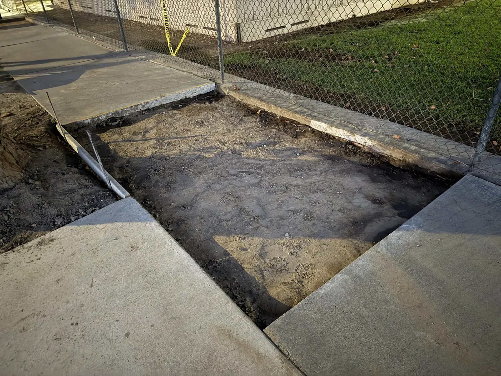 Section of paving removed between two slabs at a fence gate, dug down to grade