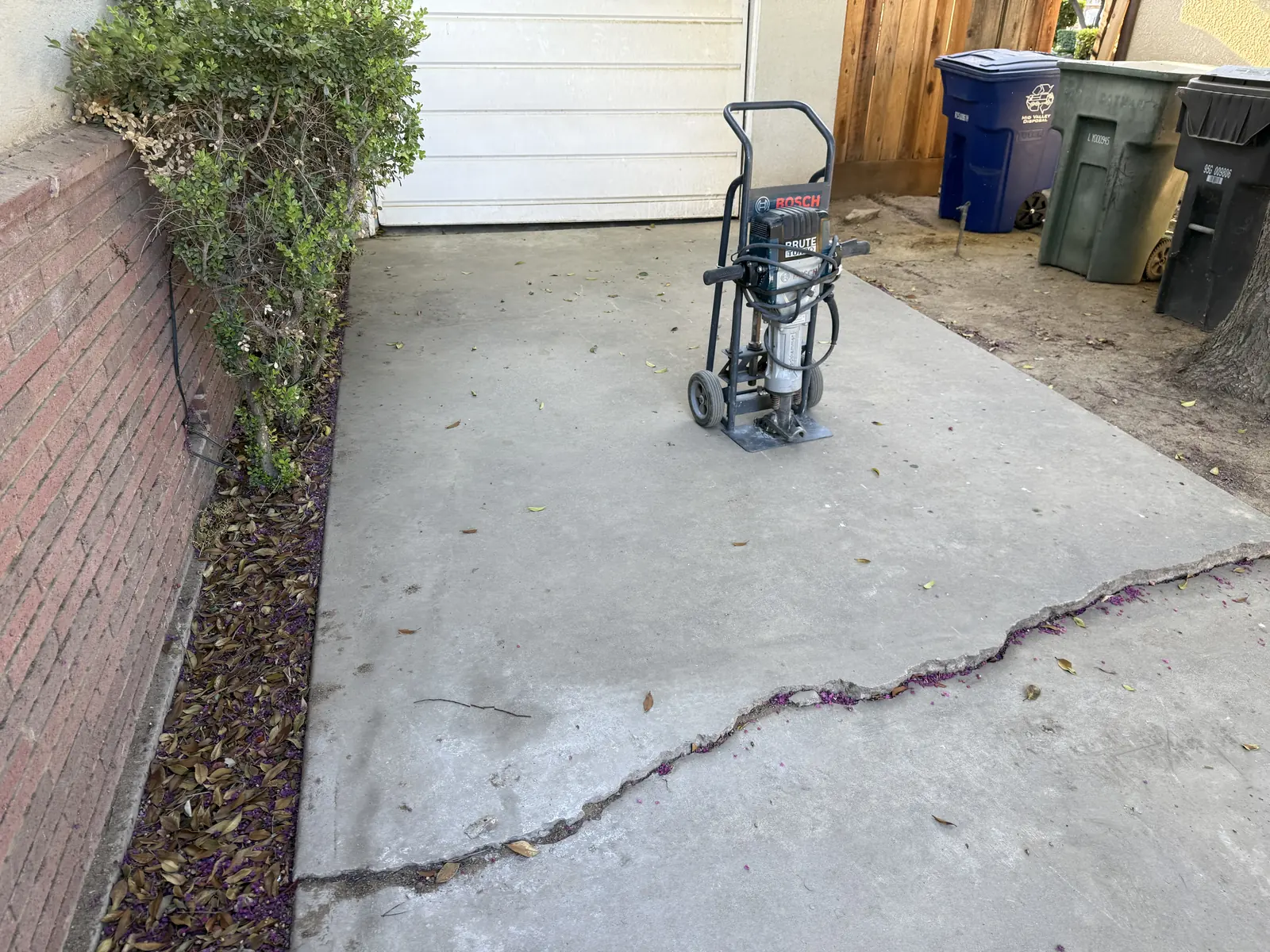 Cracked slab beside a brick planter with a demolition hammer staged on it