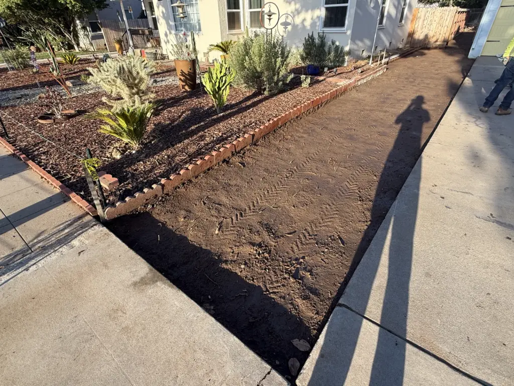 Front planting bed raked smooth behind its brick edge, soil ready for the finish grade